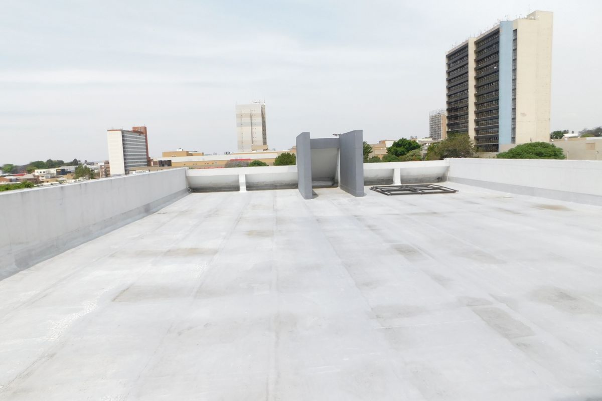 A view of the flat rooftop area of the office building, featuring a parapet wall and access structure with surrounding city skyline views.