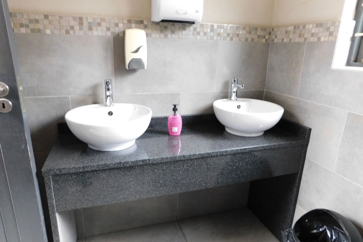 Commercial bathroom featuring a double vanity with granite countertop, dual vessel sinks, chrome faucets, and modern grey wall tiling.