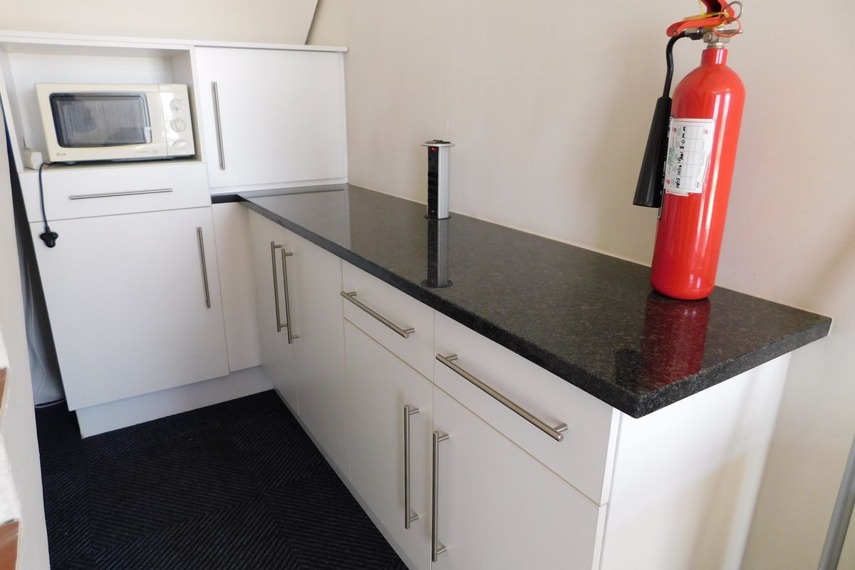A compact office kitchenette featuring white cabinetry, a dark granite countertop, and a built-in power outlet.