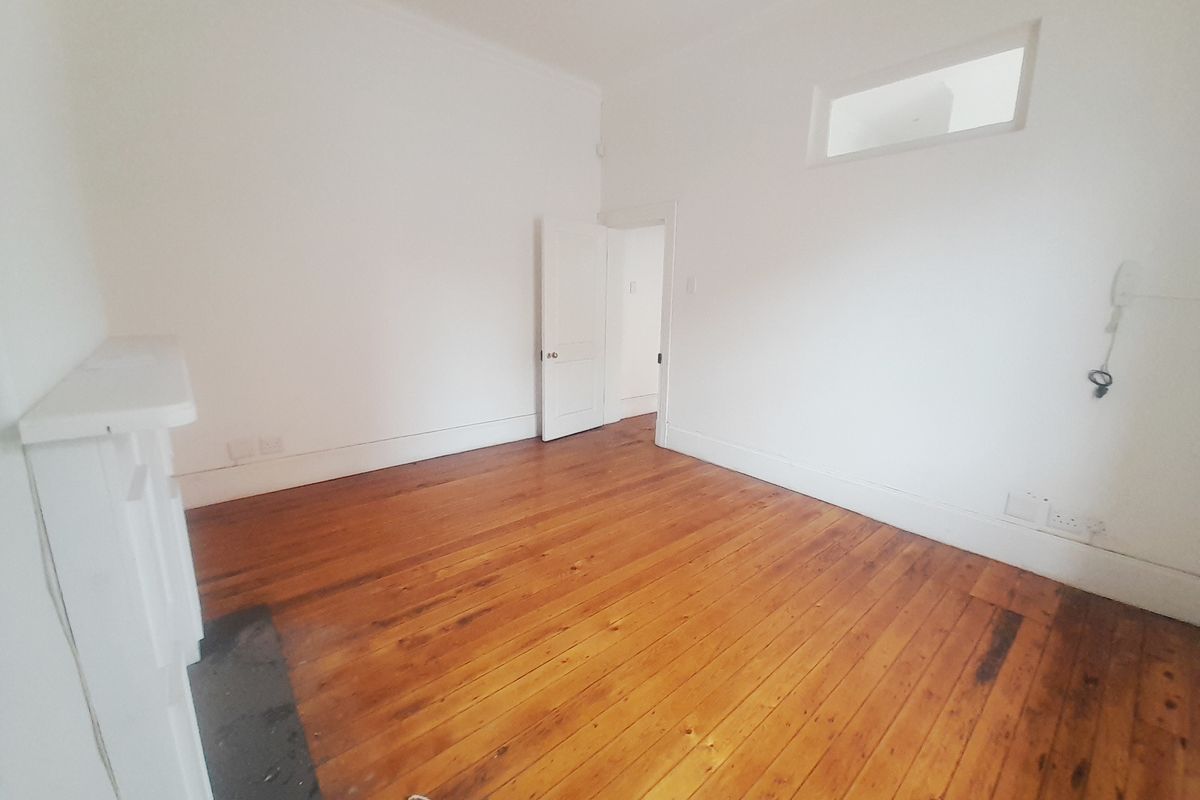 A bright, empty office space featuring polished timber flooring, a decorative fireplace mantle, and a high-level transom window for natural light.
