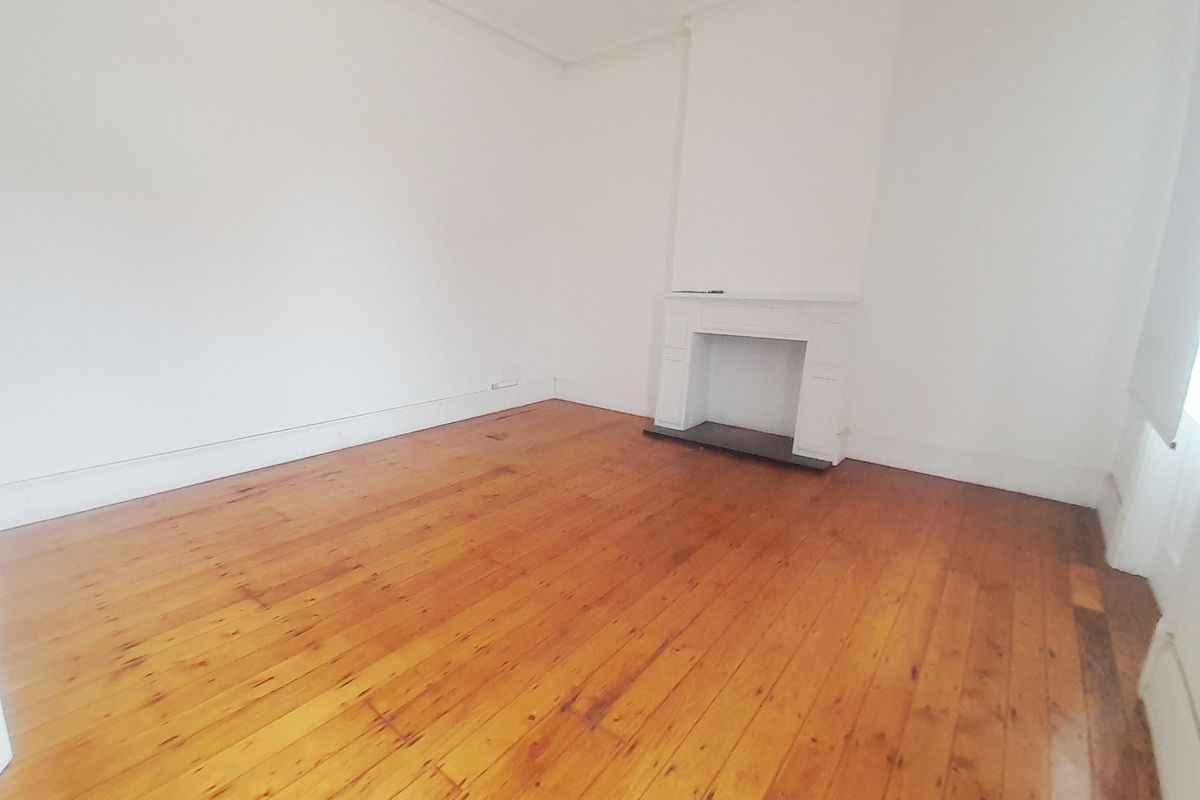 A bright, empty office space featuring polished timber flooring and a classic fireplace mantle, offering a clean and versatile work environment.