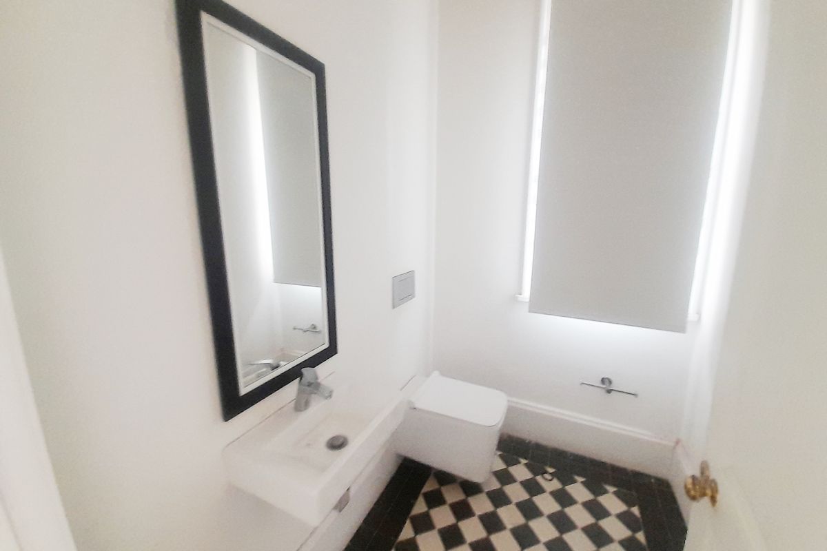 A compact office restroom featuring a wall-mounted basin, a modern toilet, and classic black and white checkered floor tiling.