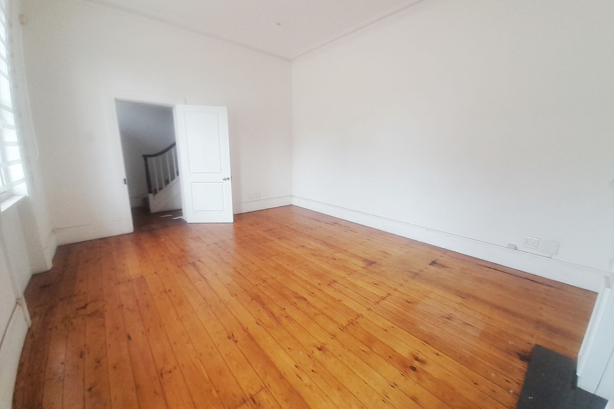 A bright, empty office space featuring polished timber flooring, white walls, and a doorway leading to an internal staircase.