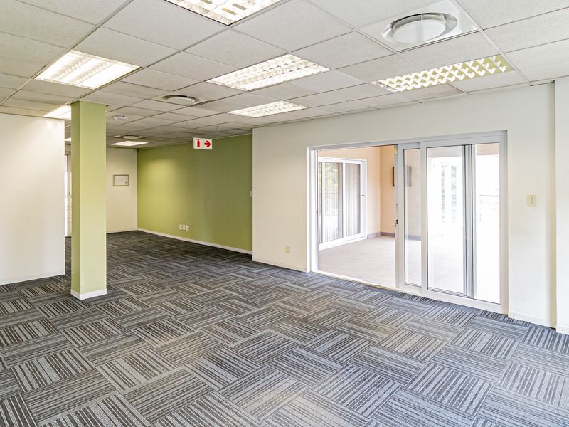 Spacious open-plan office area featuring carpet tiles, suspended ceilings with recessed lighting, and sliding glass doors leading to an outdoor space.