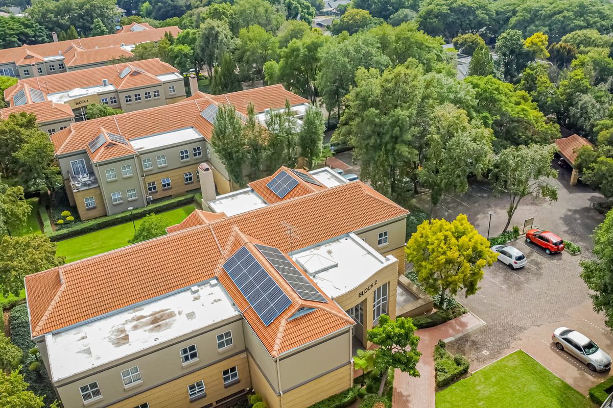 Aerial view of a multi-block office complex featuring tiled roofs, integrated solar panels, paved parking areas, and mature landscaped surroundings.