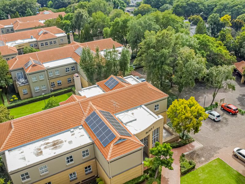 Aerial view of a multi-block office complex featuring tiled roofs, integrated solar panels, paved parking areas, and mature landscaped surroundings.