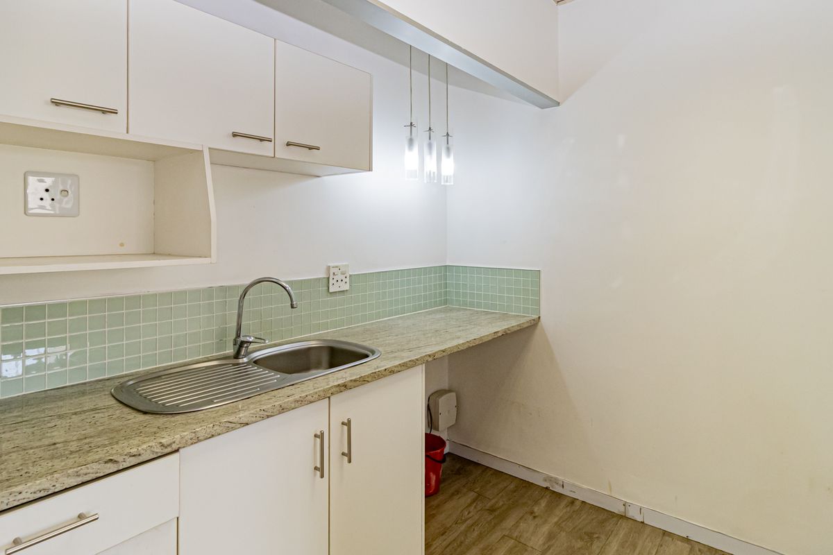 A compact kitchen area featuring white cabinetry, a stone-look laminate countertop, stainless steel sink, and a light green tiled backsplash.