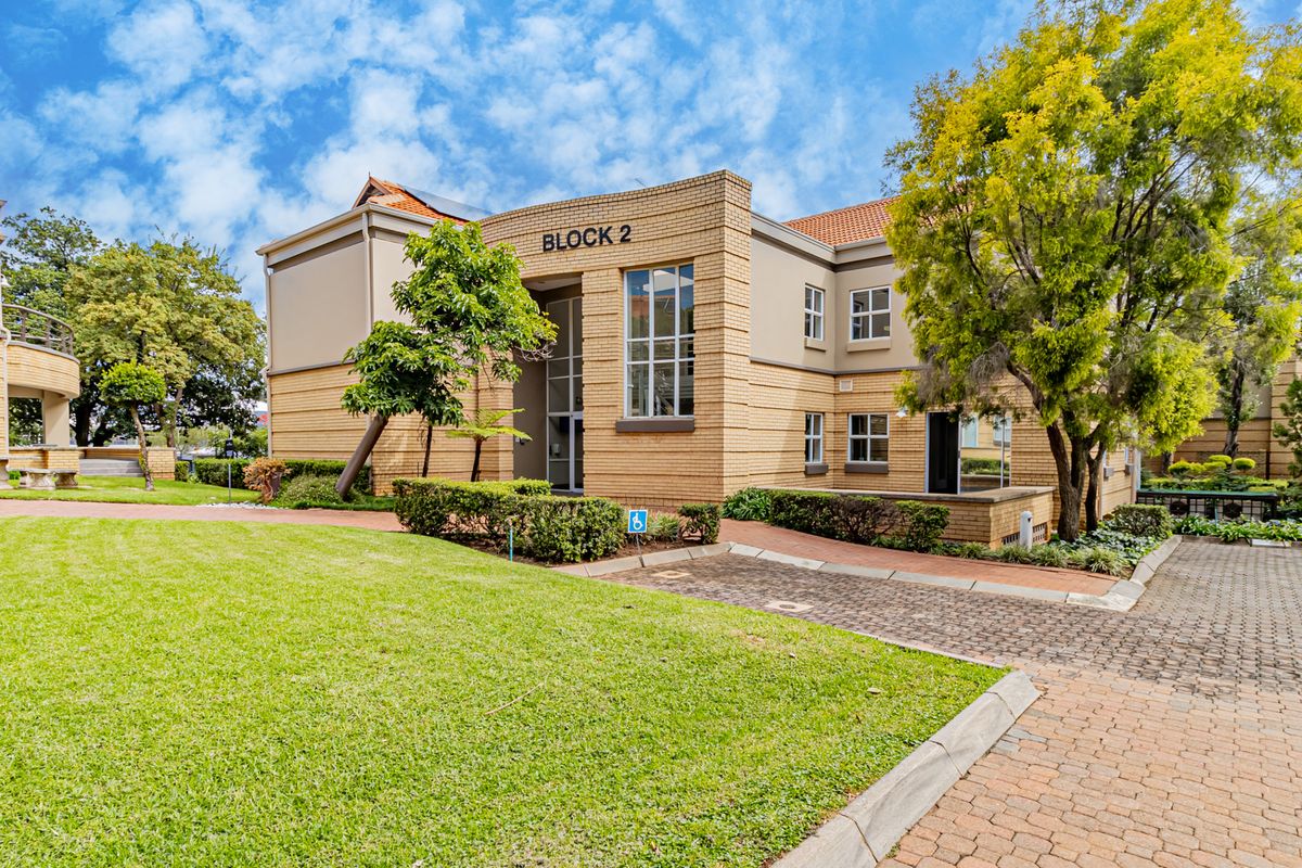 A well-maintained office building facade featuring brick construction, landscaped grounds, and paved access paths within a professional office park setting.