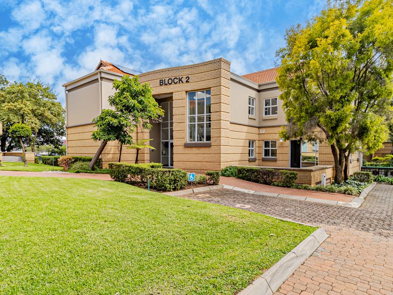 A well-maintained office building facade featuring brick construction, landscaped grounds, and paved access paths within a professional office park setting.