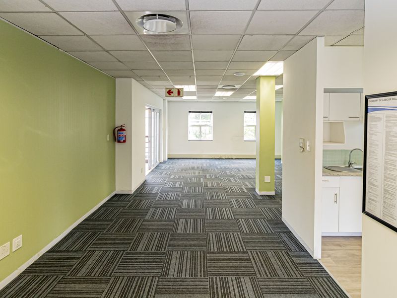 Open-plan office space featuring carpet tiles, a suspended ceiling with recessed lighting, and a small integrated kitchenette area.