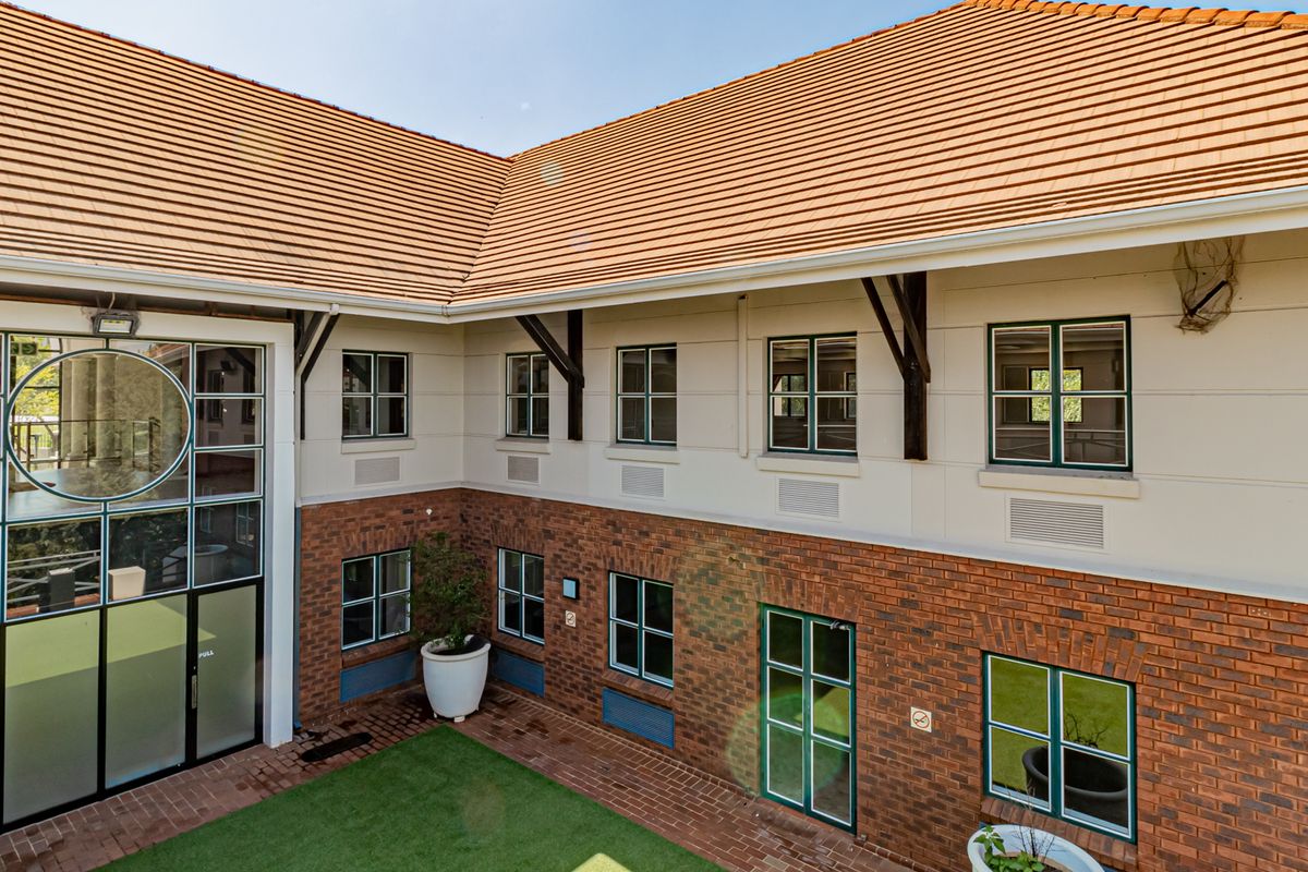 An elevated view of the office building courtyard, featuring a brick and plaster facade, tiled roof, and large glass entrance.
