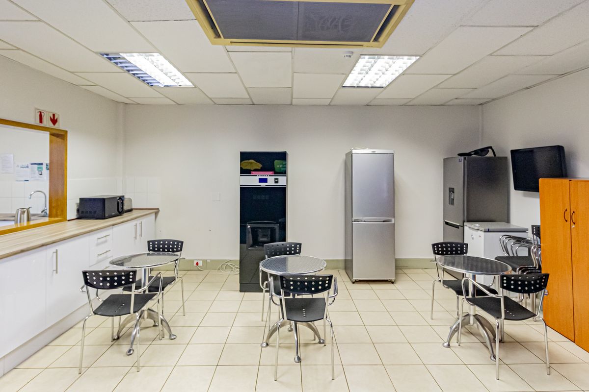 A functional office breakroom featuring a kitchenette with white cabinetry, tiled flooring, and recessed fluorescent lighting.