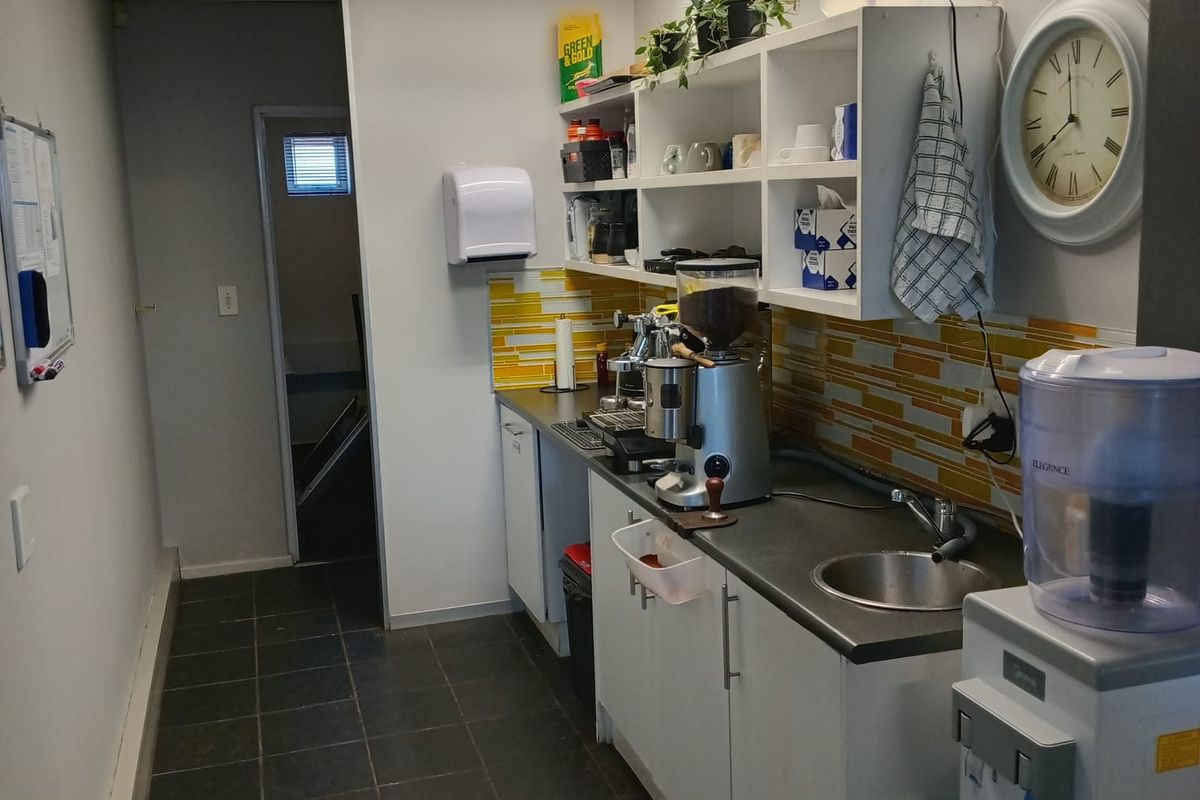 A functional office kitchenette featuring built-in cabinetry, a stainless steel sink, tiled backsplash, and recessed ceiling lighting.