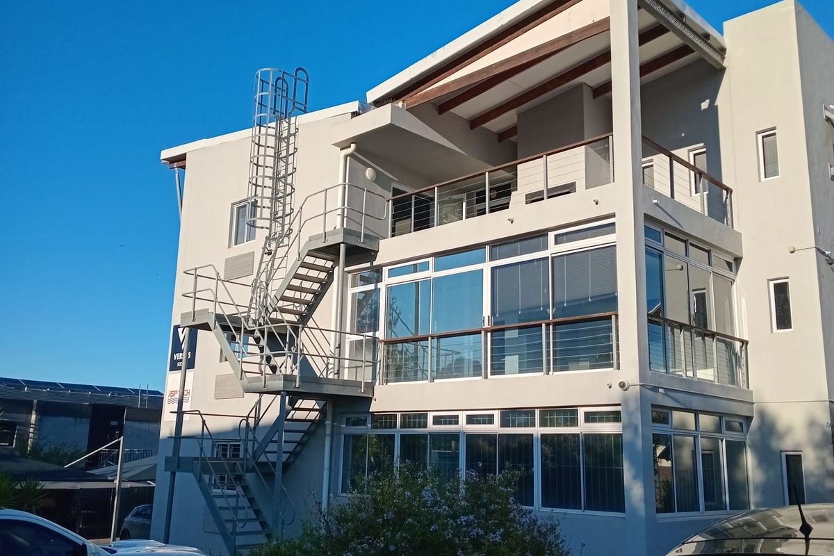 Exterior view of a modern multi-story office building featuring large glass windows, a metal fire escape staircase, and a covered balcony area.