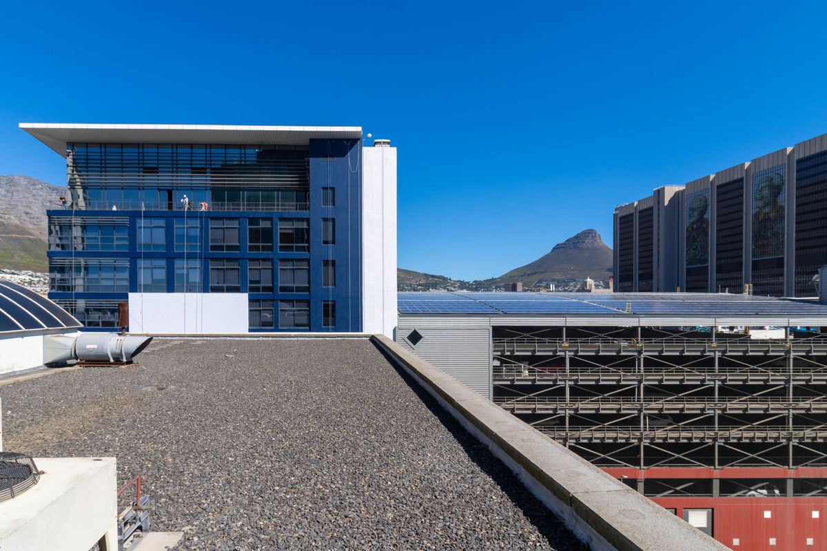 Elevated view from a commercial rooftop overlooking surrounding office buildings, parking structures, and distant mountain scenery.