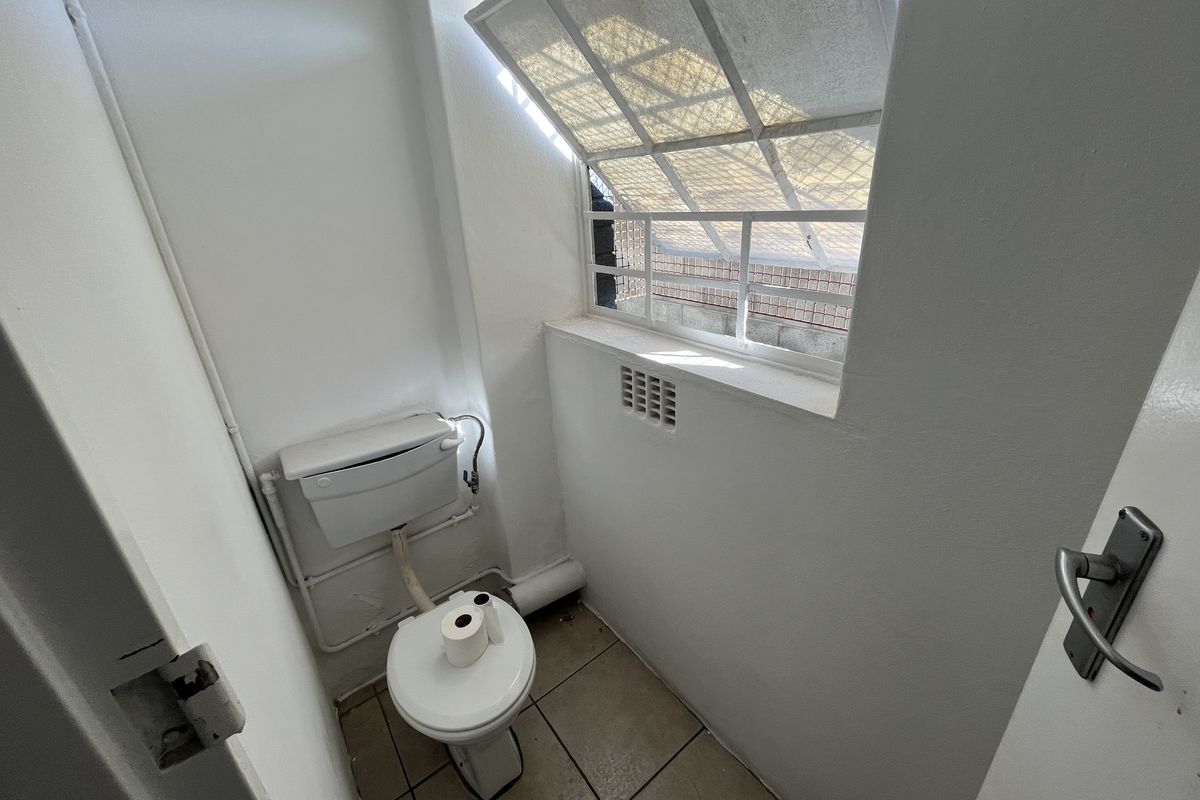 A compact, functional restroom featuring a standard toilet, tiled flooring, and a small window with security bars.