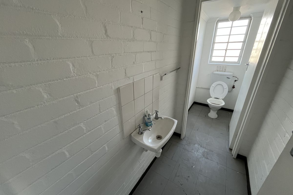 A functional industrial-style bathroom featuring a wall-mounted basin and a separate toilet cubicle with a window.