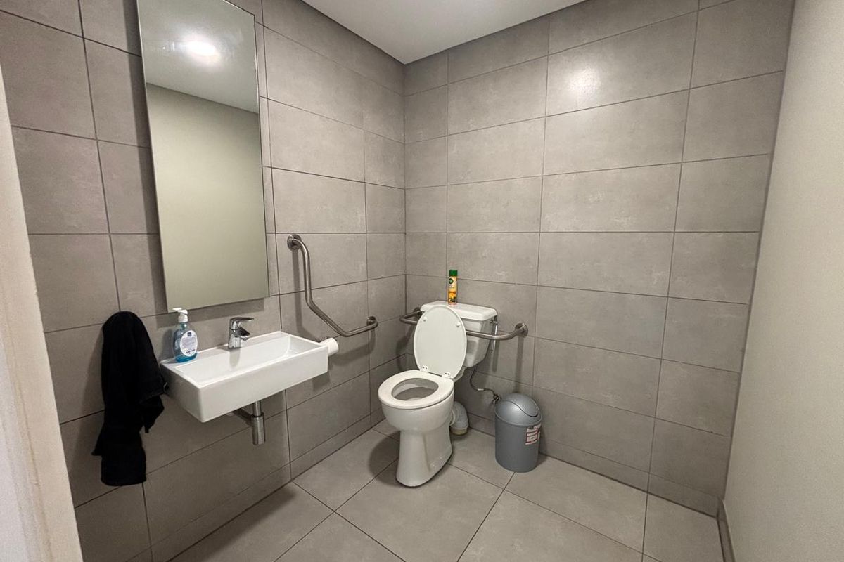 A modern, accessible bathroom featuring grey floor-to-ceiling tiling, a wall-mounted basin, and stainless steel grab rails for accessibility.