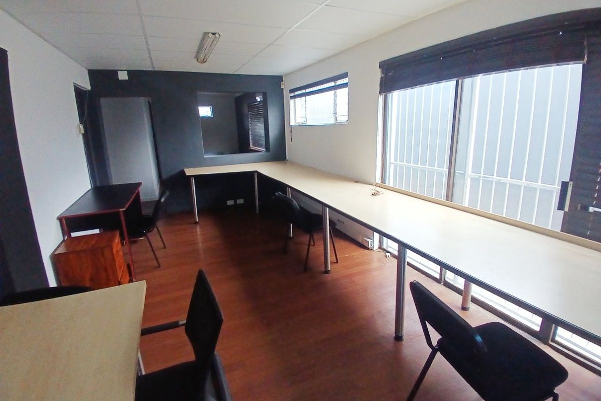 A functional office space featuring built-in desk workstations, large windows with security bars, and wood-look laminate flooring.