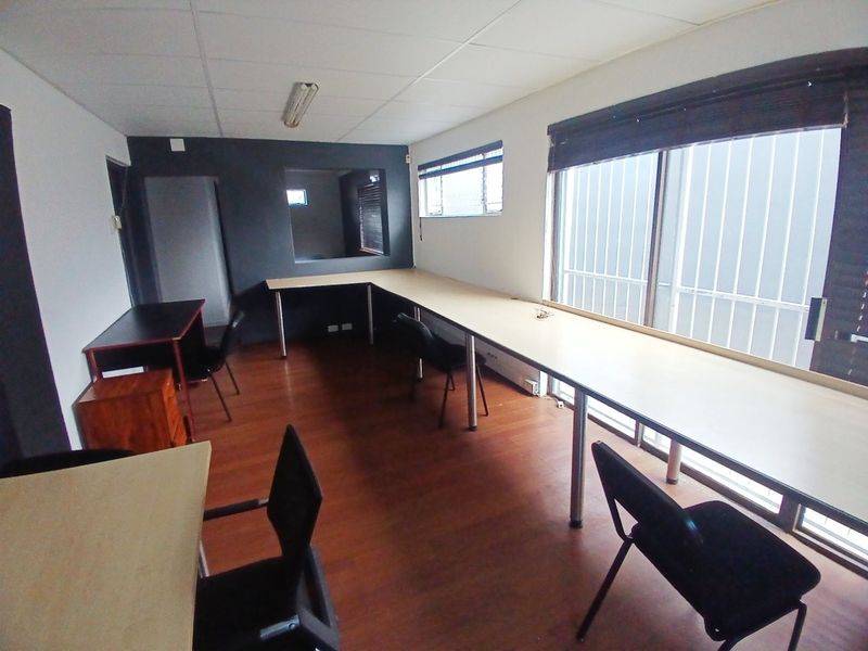 A functional office space featuring built-in desk workstations, large windows with security bars, and wood-look laminate flooring.