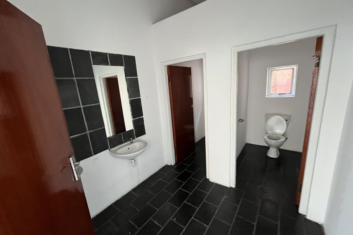 A functional bathroom area featuring a wall-mounted basin with tiled splashback and a separate toilet cubicle with dark floor tiling.