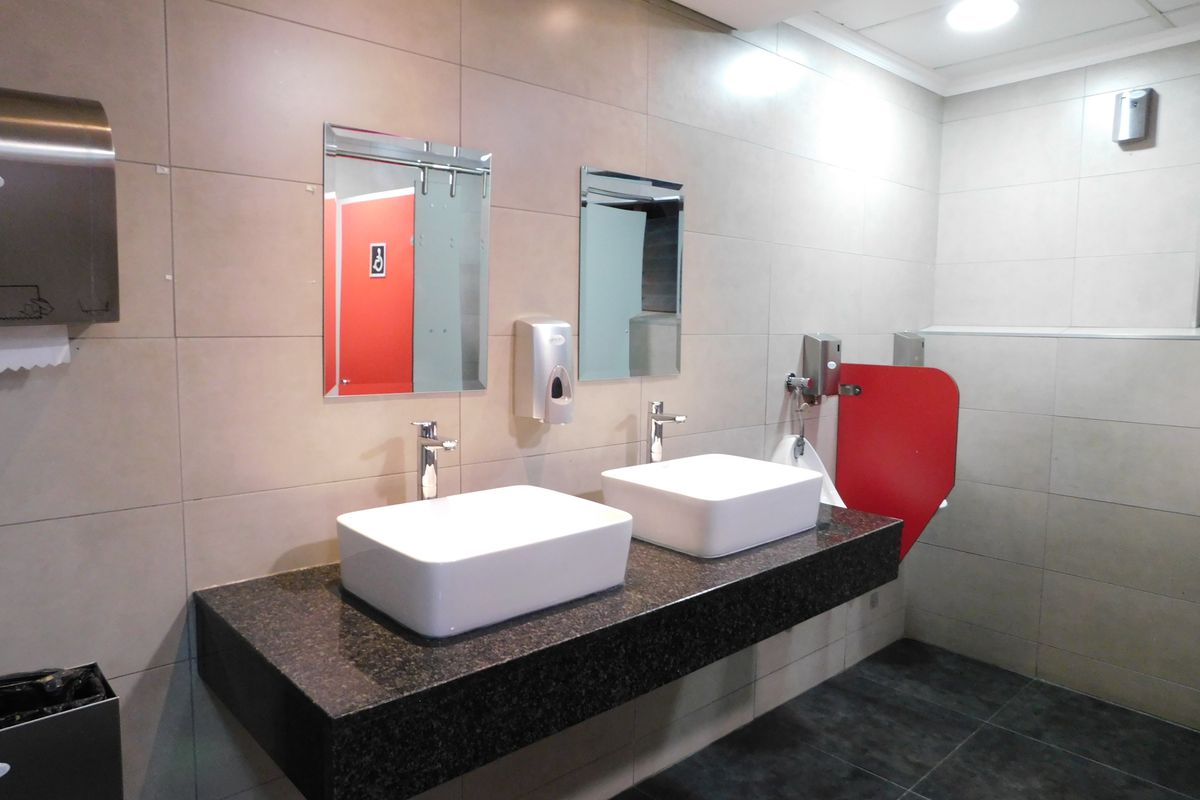 Modern office restroom featuring a floating granite vanity with dual vessel sinks, tiled walls, and contemporary fixtures.