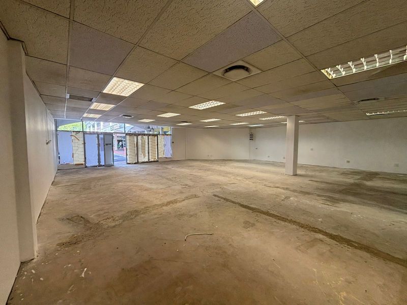 A vacant open-plan retail space featuring a suspended ceiling, recessed lighting, and concrete flooring, ready for custom fit-out.