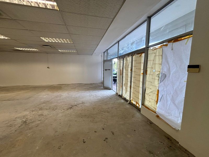 An empty retail space featuring a suspended ceiling, recessed lighting, and large glass storefront windows, currently awaiting flooring and interior finishing.