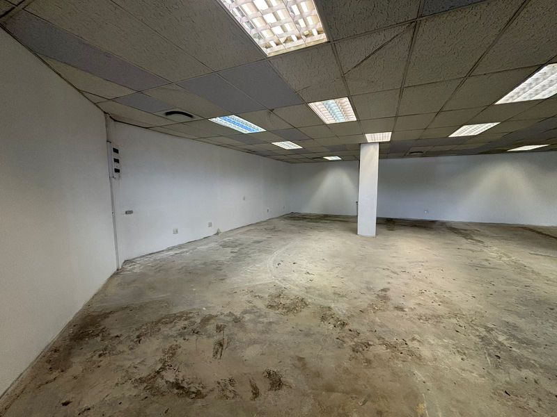 An empty, open-plan retail space featuring a suspended ceiling with recessed lighting, a central structural column, and unfinished concrete flooring.
