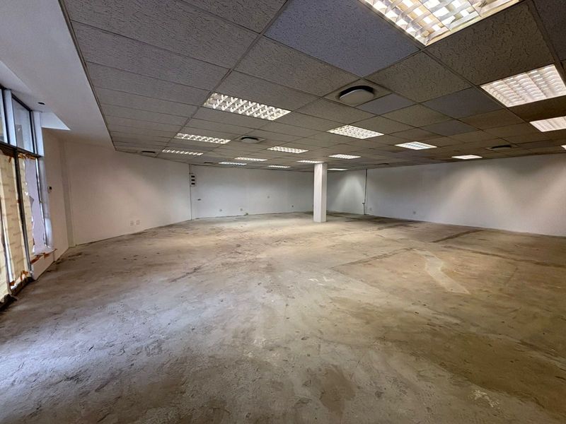 A vacant open-plan retail space featuring a suspended ceiling, recessed lighting, and large glass storefront windows, ready for custom fit-out.