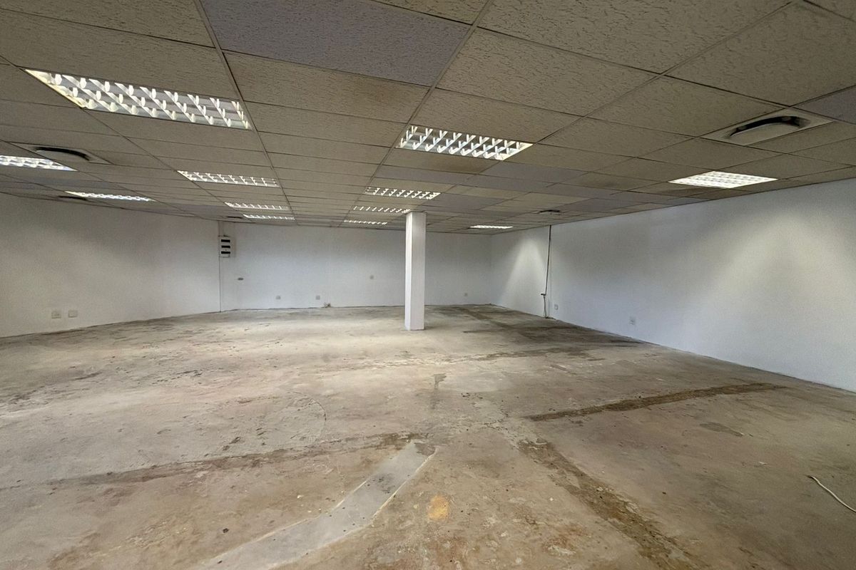 An expansive, empty open-plan retail space featuring a suspended ceiling with recessed lighting, a central support column, and unfinished concrete flooring.