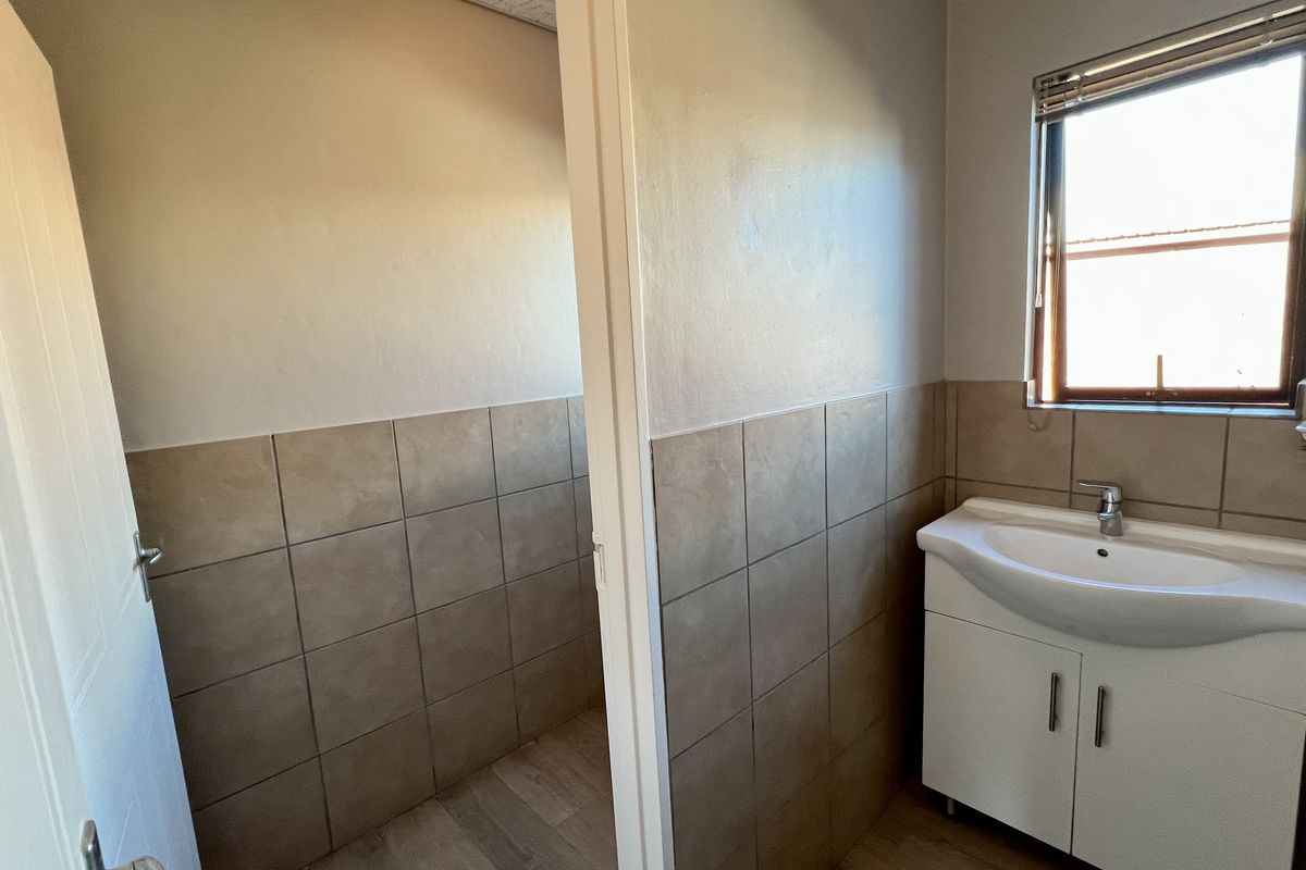 A functional office bathroom featuring a vanity basin, tiled splashbacks, and a window for natural light.