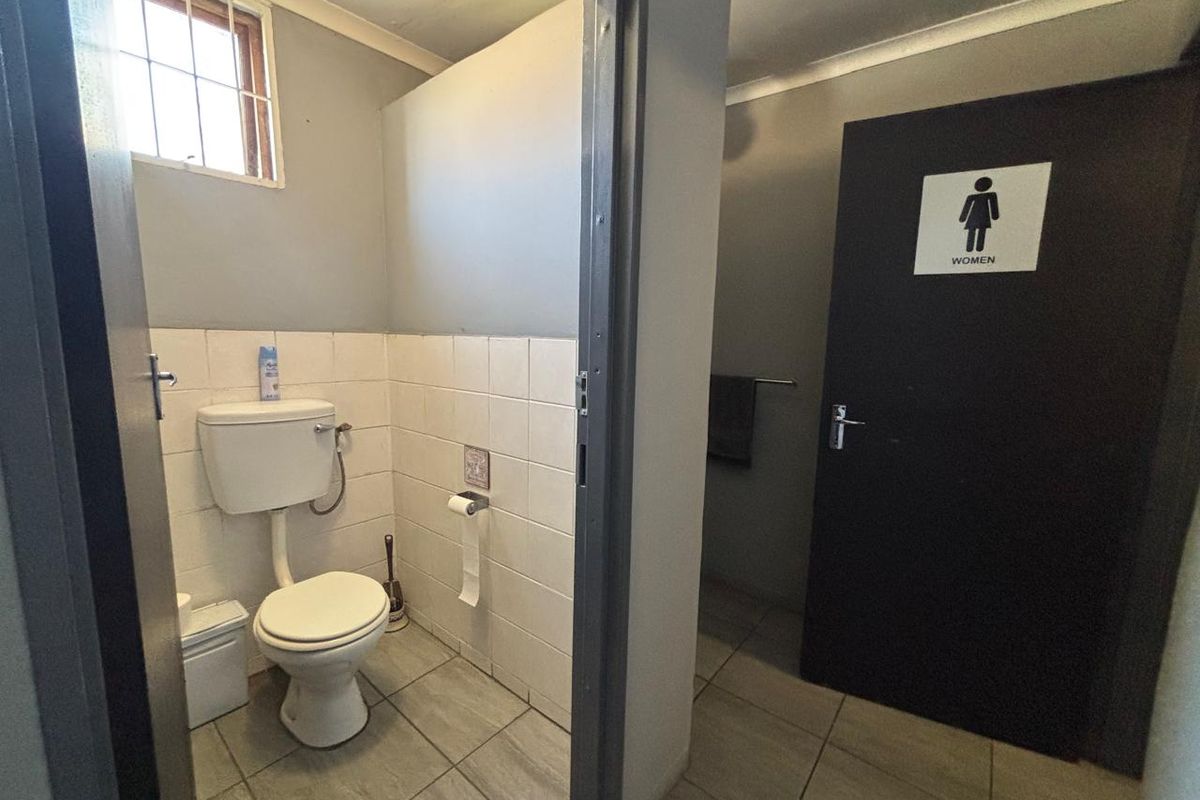 A functional office restroom facility featuring tiled flooring, wall-mounted toilet, and a designated women's entrance door.