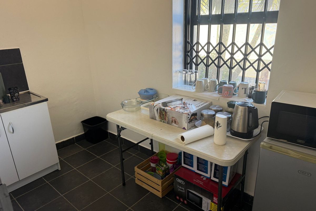 A compact kitchenette area featuring a small sink unit, tiled flooring, and a security gate on the window.