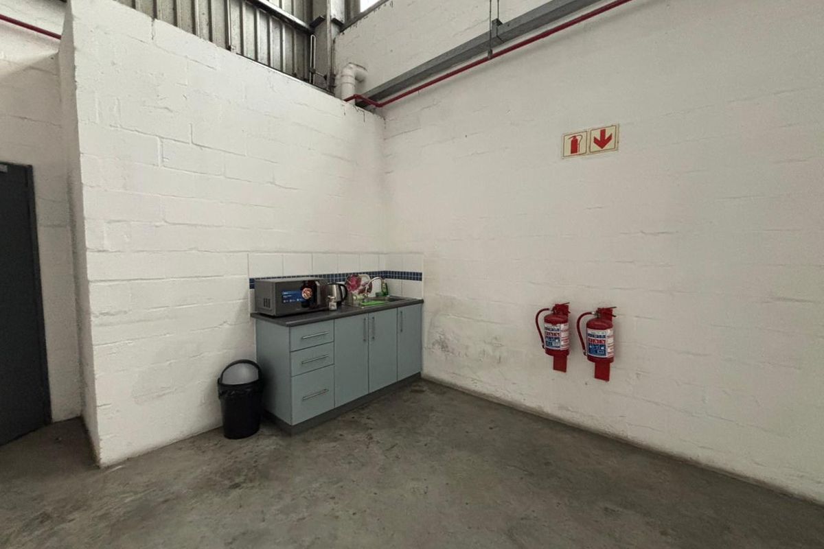 A functional kitchenette area within an industrial space, featuring built-in cabinetry, a sink, and wall-mounted fire safety equipment.
