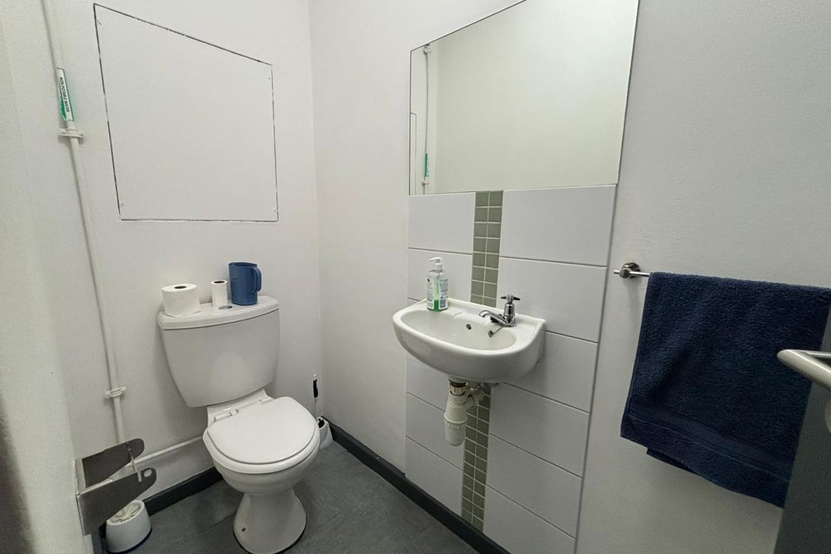 A functional industrial-style restroom featuring a wall-mounted basin, a standard toilet, and a large wall mirror with tiled splashback.