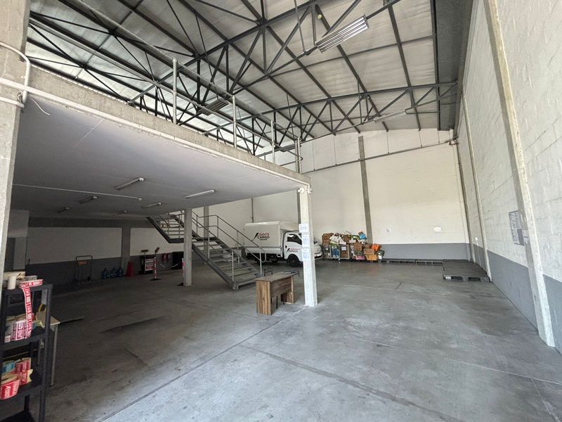 Spacious industrial warehouse featuring a high-volume ceiling, concrete flooring, and a mezzanine level accessible via a metal staircase.