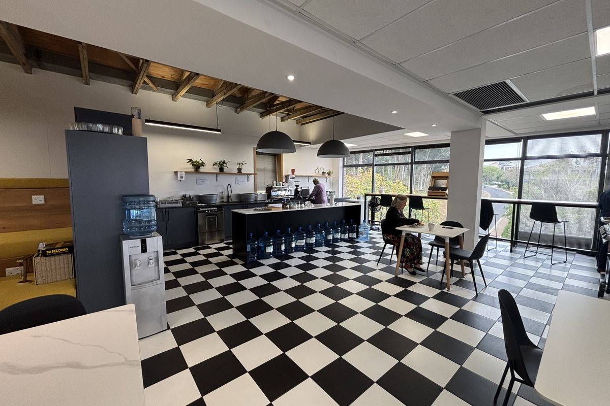 A modern office breakroom featuring a kitchenette with dark cabinetry, a central island, and distinctive black and white checkered flooring.
