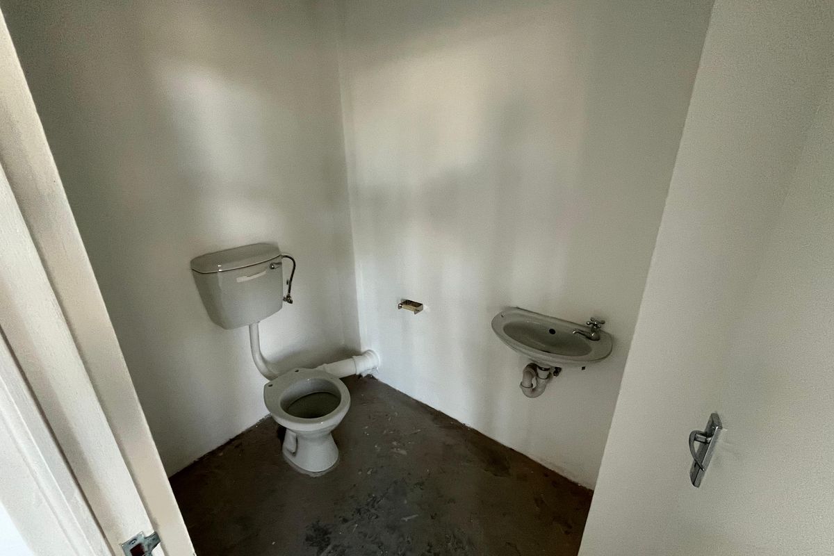 A small, basic restroom featuring a wall-mounted basin and a standard toilet, currently in a shell-like condition requiring flooring and wall finishing.