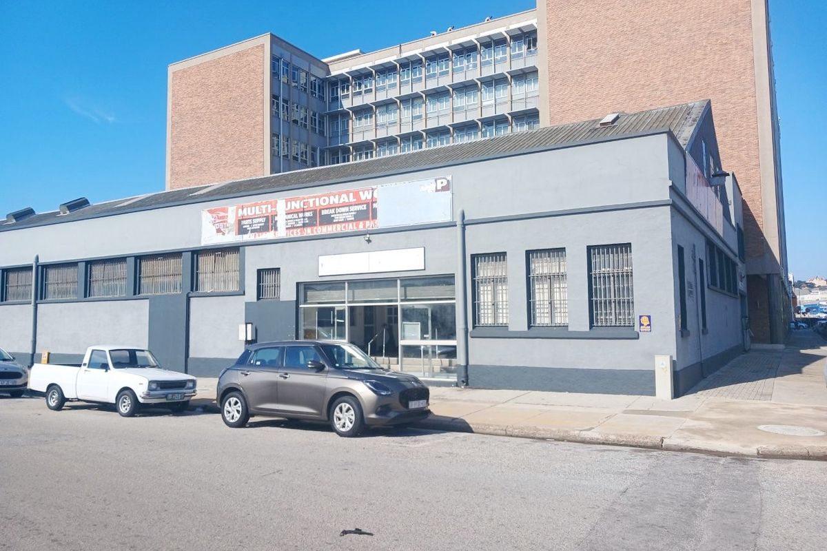 Industrial building facade featuring large windows with security bars, a prominent entrance, and signage, situated on a street-level corner plot.