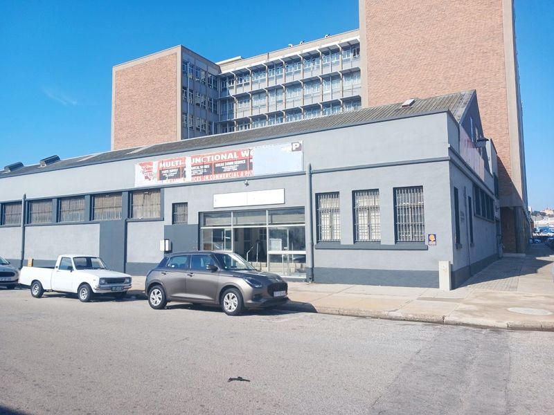 Industrial building facade featuring large windows with security bars, a prominent entrance, and signage, situated on a street-level corner plot.