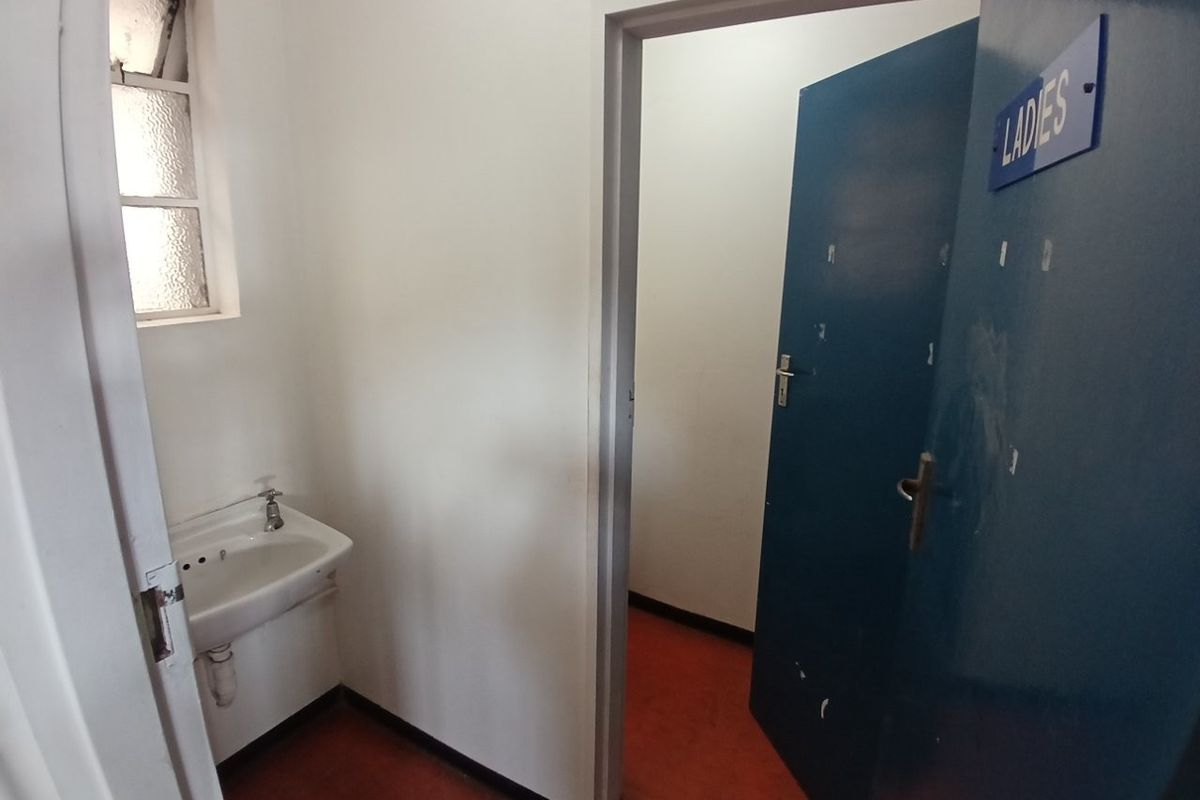 A functional industrial restroom facility featuring a wall-mounted basin, tiled window, and designated ladies' access door.