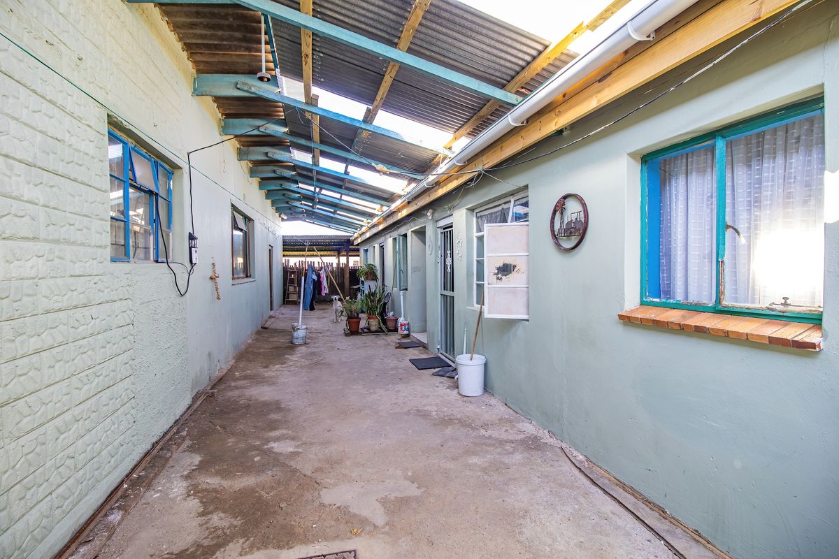 A covered outdoor walkway or courtyard area featuring concrete flooring and a corrugated iron roof structure, providing access to multiple building entrances.