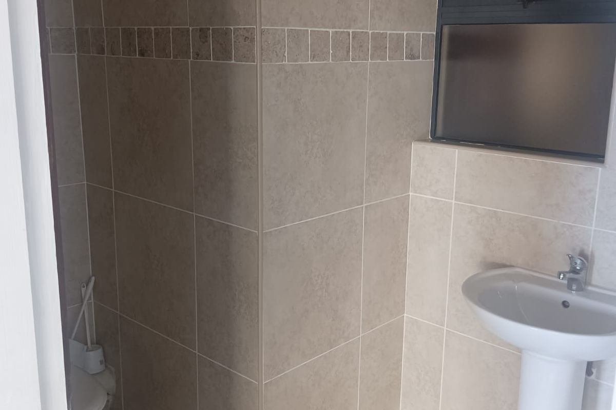 A clean, functional office restroom featuring neutral wall and floor tiling, a pedestal basin, and a frosted glass window for privacy.