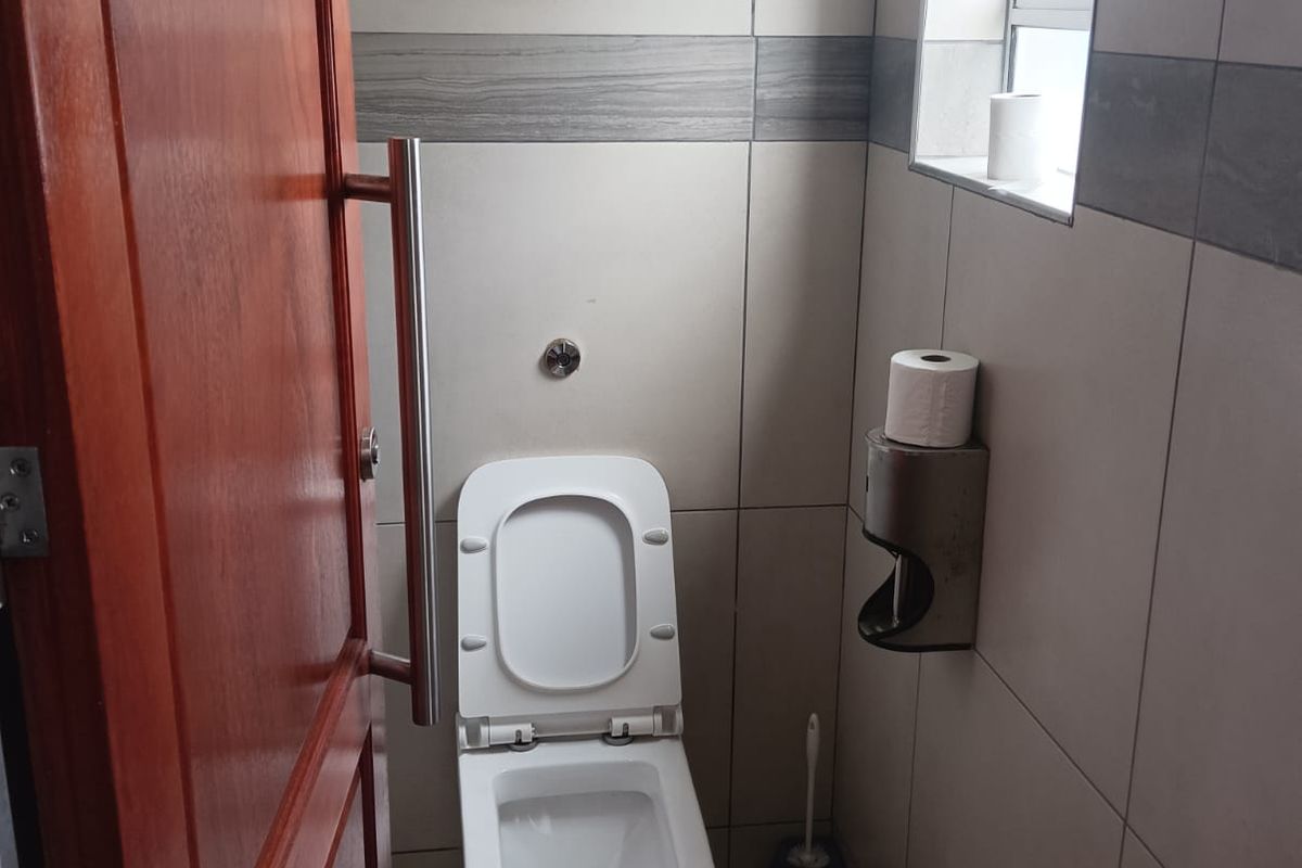 A compact office restroom featuring full-height wall tiling, a modern toilet, and a window for ventilation.