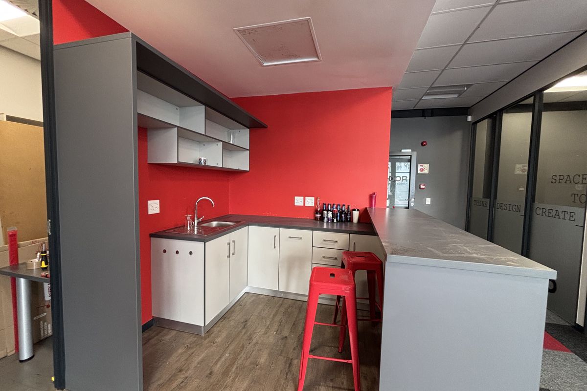A compact office kitchenette featuring built-in cabinetry, a stainless steel sink, and a breakfast bar counter.