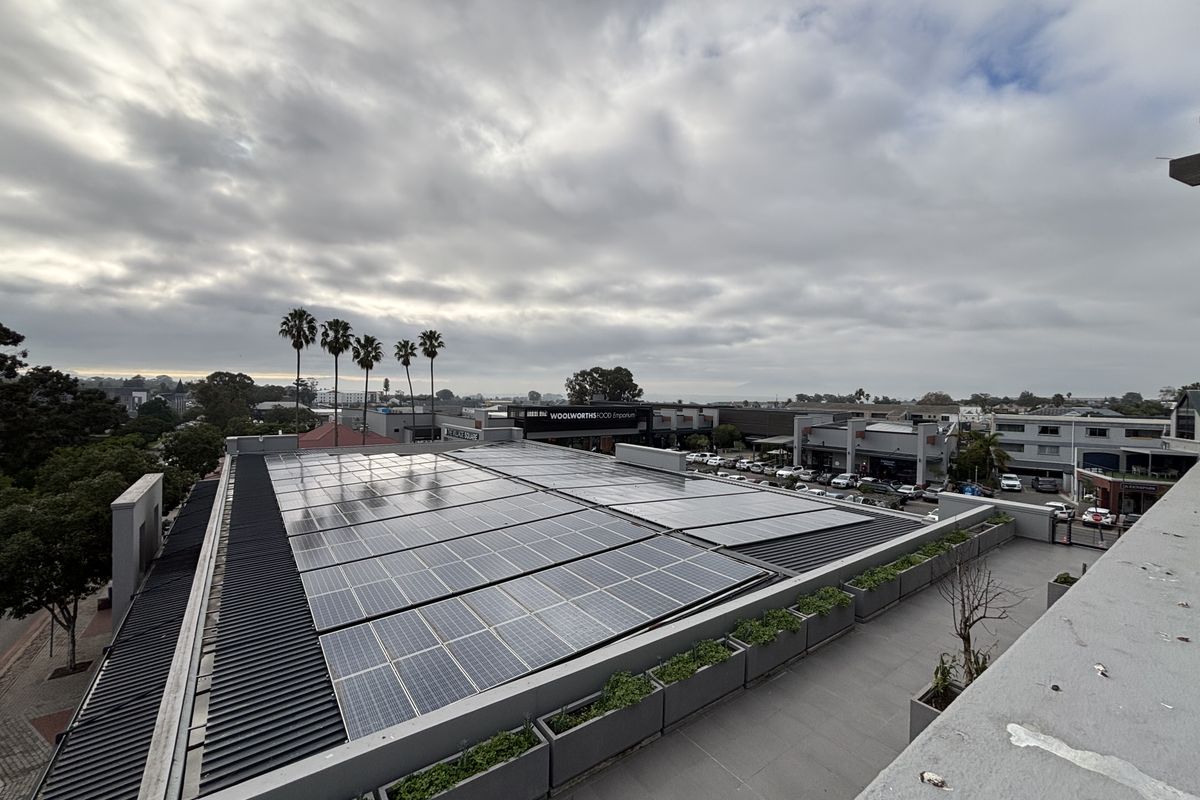 Elevated view of the office building rooftop featuring an extensive solar panel installation and integrated concrete planter boxes.