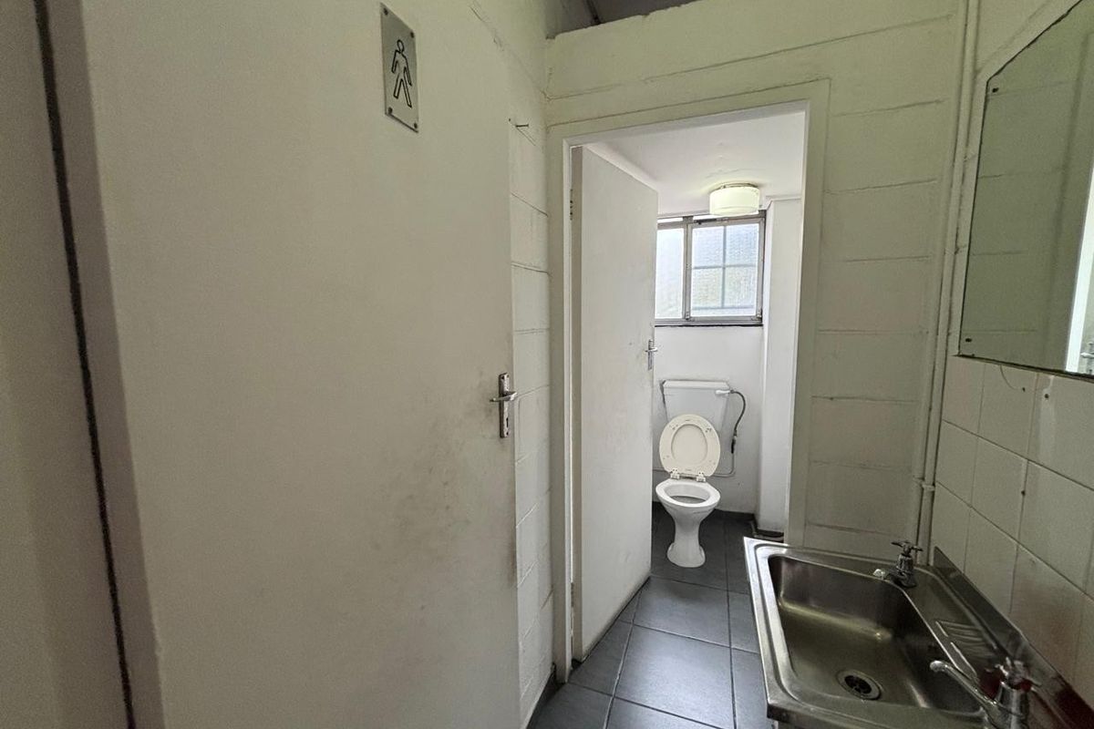 A functional industrial-style restroom facility featuring a stainless steel basin, tiled flooring, and a separate toilet cubicle with a window.