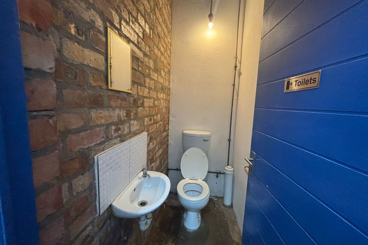 A functional industrial-style restroom featuring exposed brick walls, a wall-mounted basin, and a standard toilet suite.
