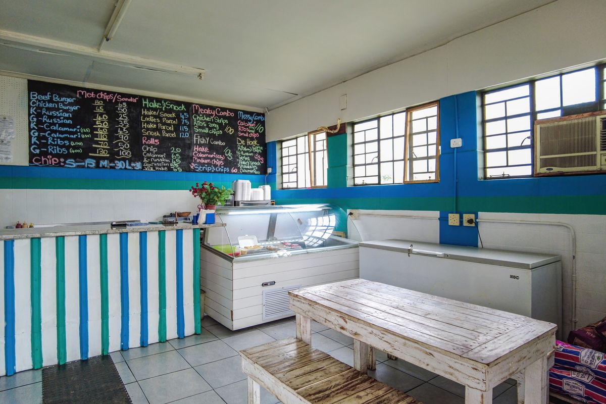 A functional commercial kitchen or takeaway service area featuring a service counter, menu board, and tiled flooring, suitable for food preparation and customer service.